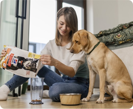 Žena sipa hranu Hill's Pet Nutrition u mjericu dok pas pažljivo gleda.